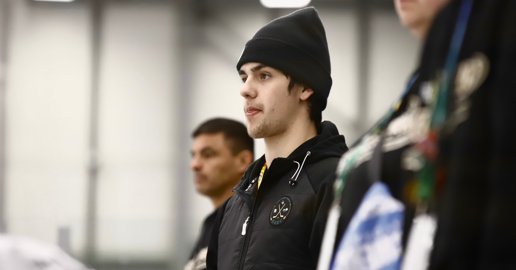 Kaden is standing wearing a black jacket and black toque. Two others stand closely beside him.