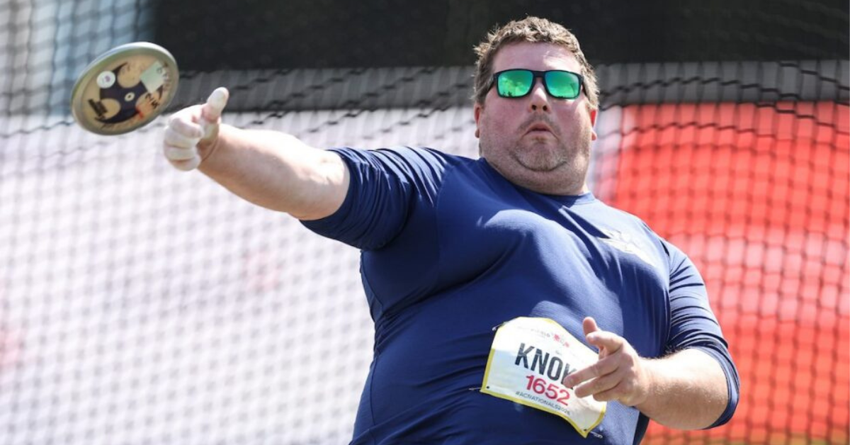Action shot of Maitlin Knoke throwing a discus. He is wearing blue lens sunglasses and a navy blue tee shirt.